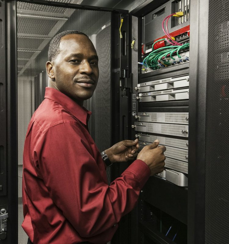 Black man technician working on computer servers in server farm.